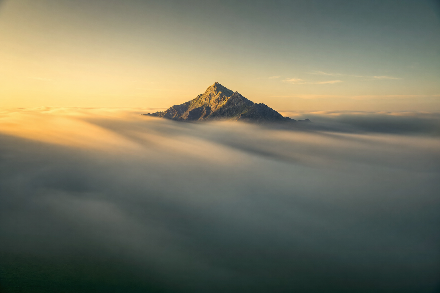 夜明けの雲海を突き抜ける山の稜線。その下には厚い雲の層が広がる